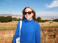 a woman wearing a blue sweater and sunglasses in front of a brick wall